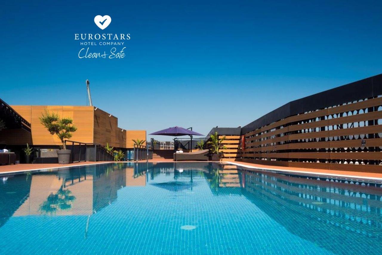 Eurostars Palace Cordoba Ngoại thất bức ảnh The photo shows an outdoor swimming pool with clear, blue water, reflecting the blue sky above. The pool area is surrounded by modern architectural features, including wooden slats and potted plants. There is also a purple umbrella providing shade. T