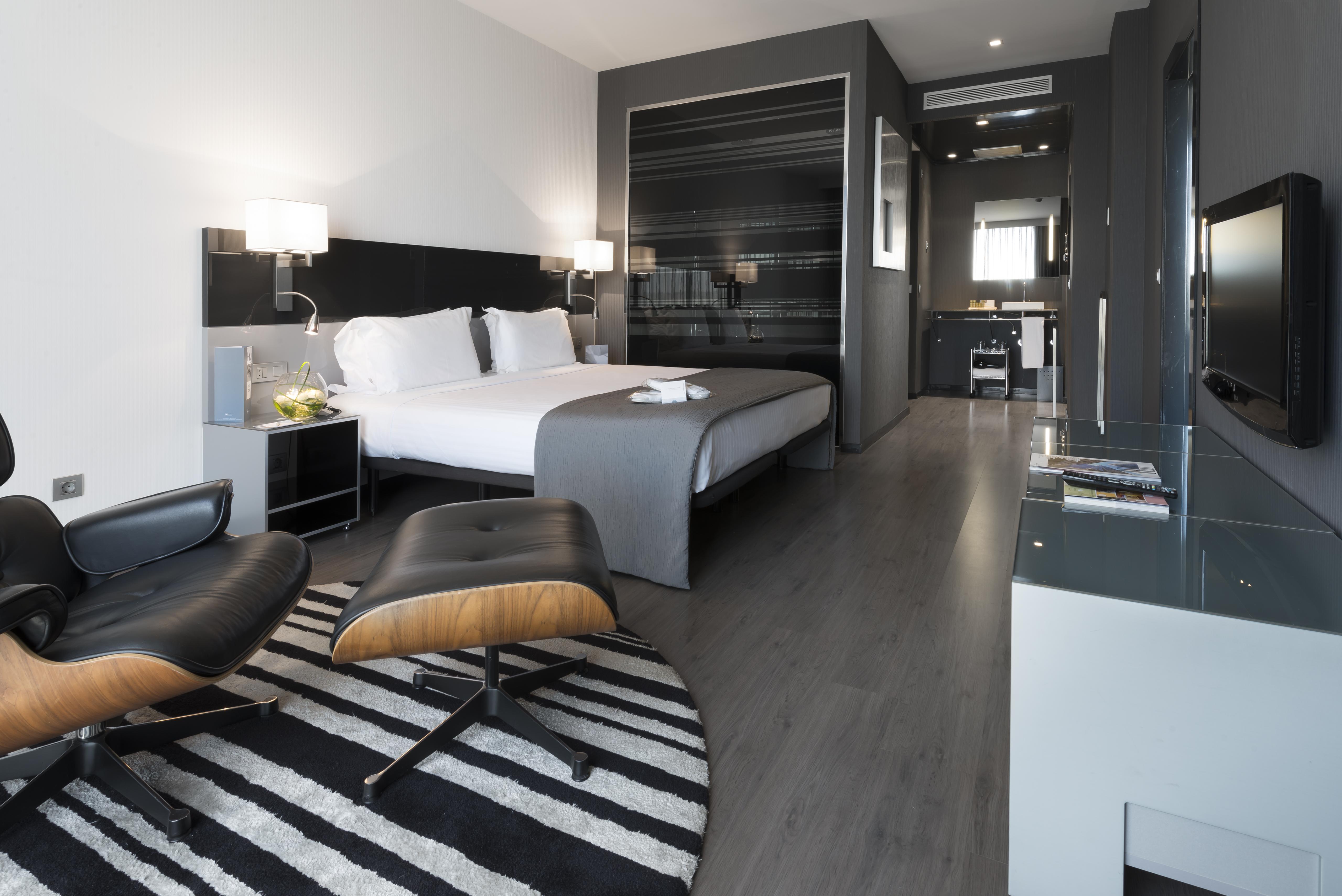 Eurostars Palace Cordoba Ngoại thất bức ảnh The photo shows a modern hotel room featuring a king-sized bed with light-colored linens and dark accent walls. There are stylish bedside tables with lamps, and a comfortable lounge chair paired with an ottoman placed on a striped rug. The room also 