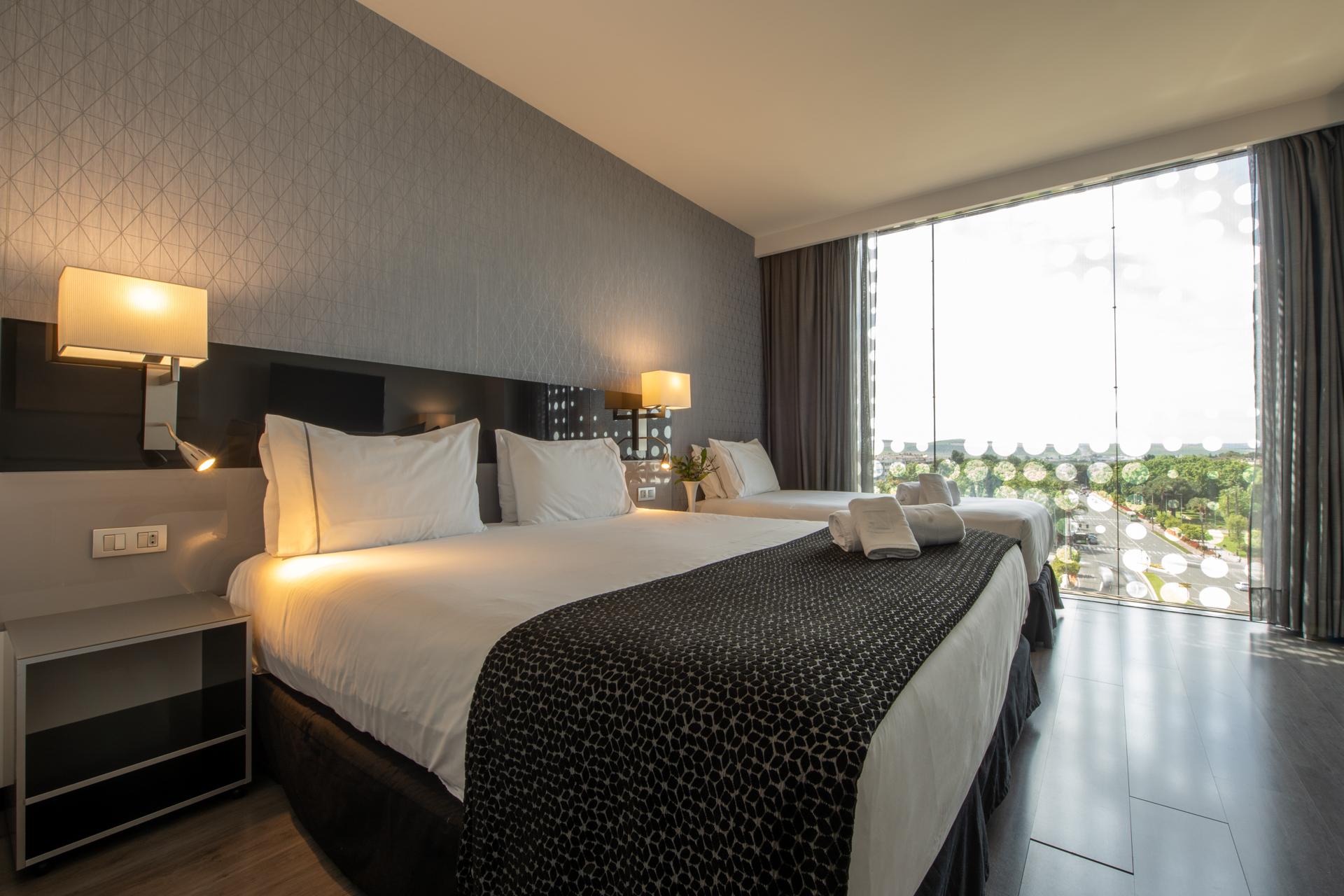 Eurostars Palace Cordoba Ngoại thất bức ảnh The photo shows a modern hotel room featuring two large beds with white linens and dark patterned bedspreads. Each bed has a set of pillows and a decorative cushion. There are bedside lamps on either side of the beds, and a contemporary piece of furn