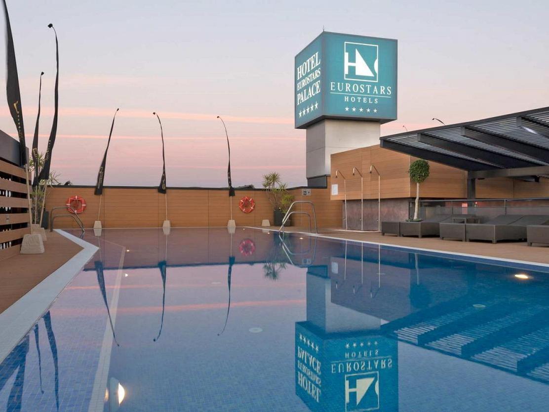 Eurostars Palace Cordoba Ngoại thất bức ảnh The image shows a hotel pool area at twilight. The pool is large and reflective, capturing the colors of the sky and surrounding features. In the background, there is a hotel sign displaying the Eurostars brand, with a modern architecture style. The 