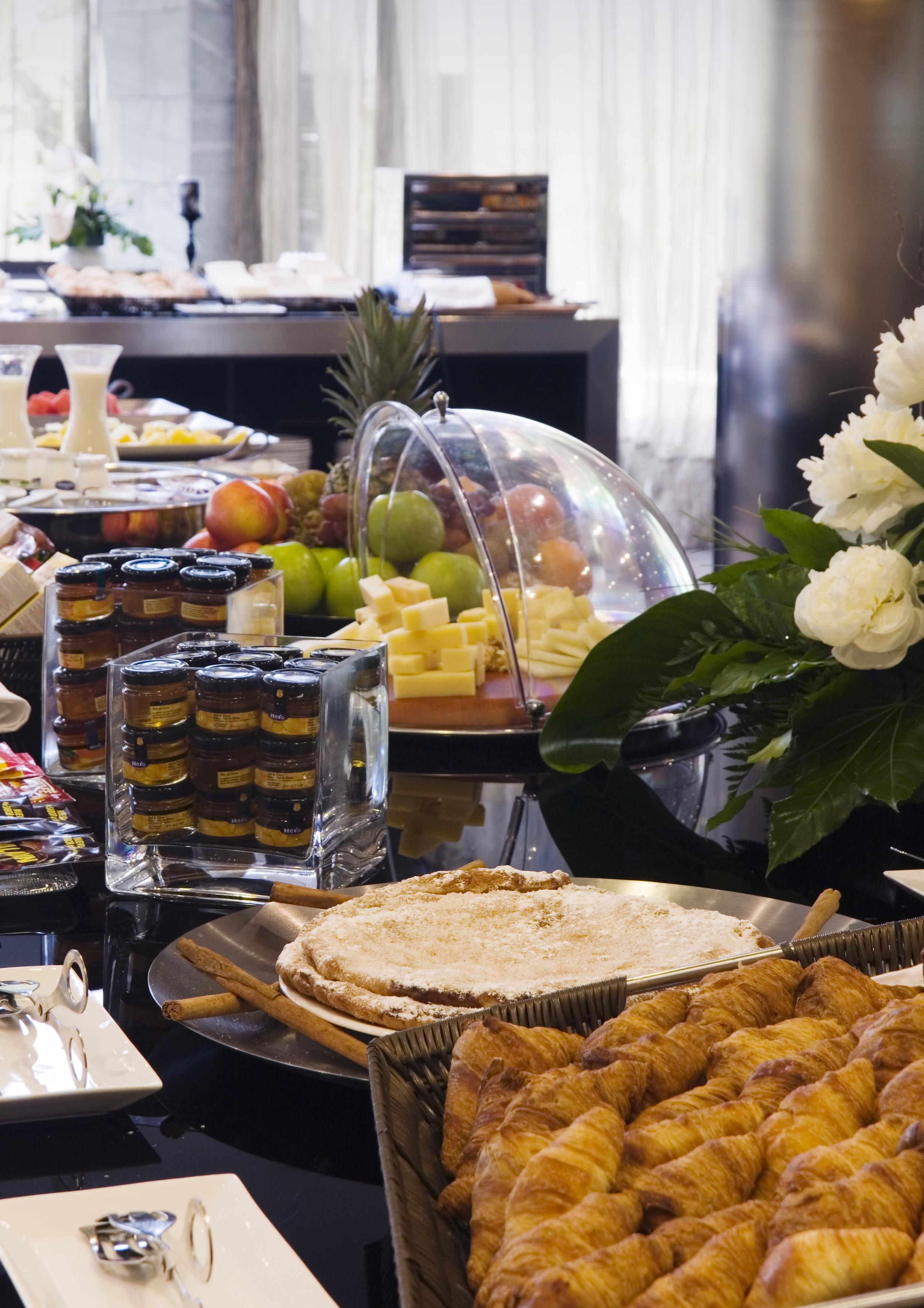 Eurostars Palace Cordoba Ngoại thất bức ảnh The photo shows a buffet-style arrangement with a variety of food items. There are fruits such as apples and grapes displayed prominently, along with a selection of cheeses presented on a wooden platter. A glass dome covers some of the items, possibl
