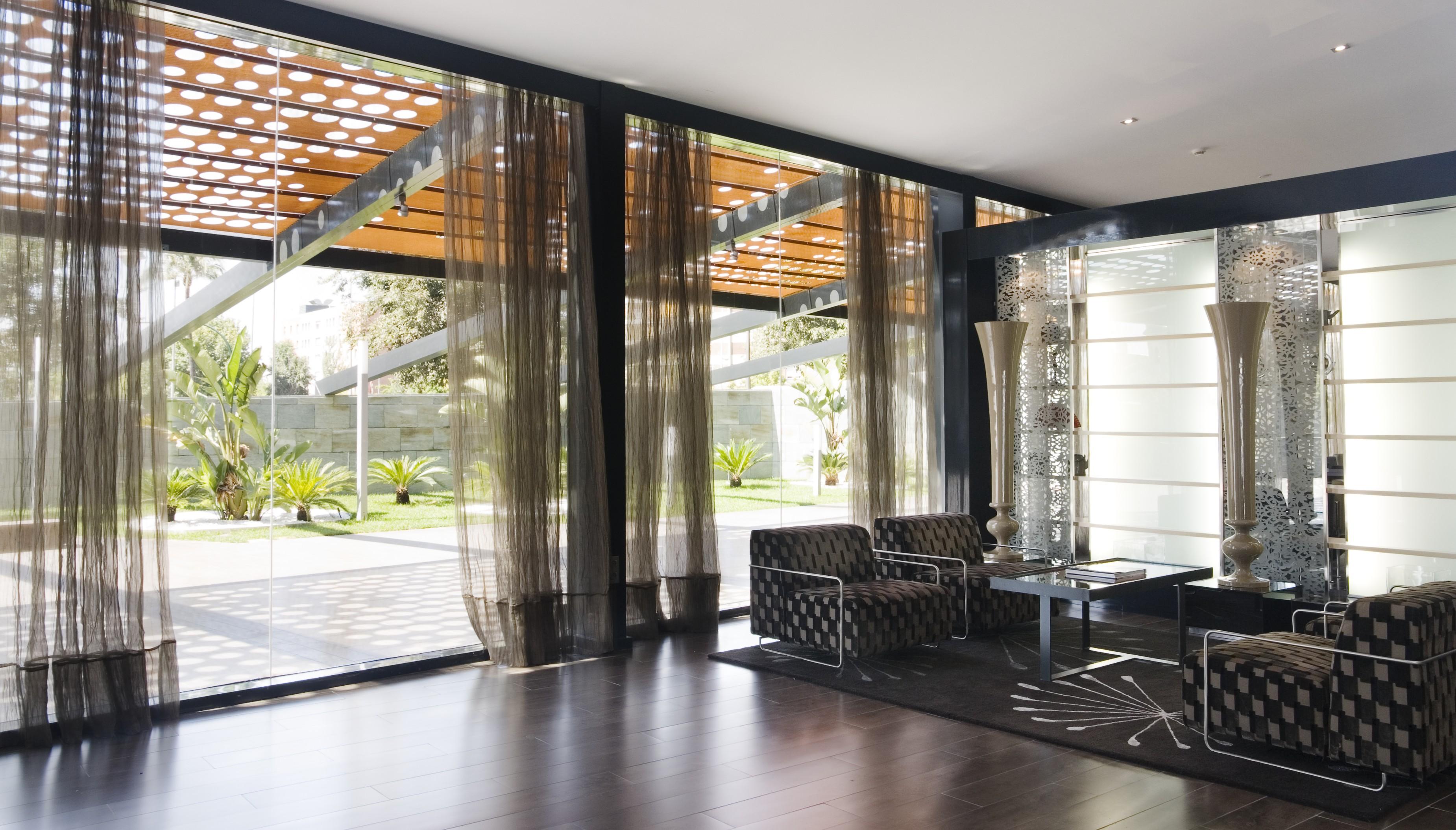 Eurostars Palace Cordoba Ngoại thất bức ảnh The photo shows a modern interior space characterized by large windows that allow natural light to flood in. The floor is made of dark wood, which contrasts with the lighter tones of the furnishings. 

In the foreground, there are two stylish chairs 