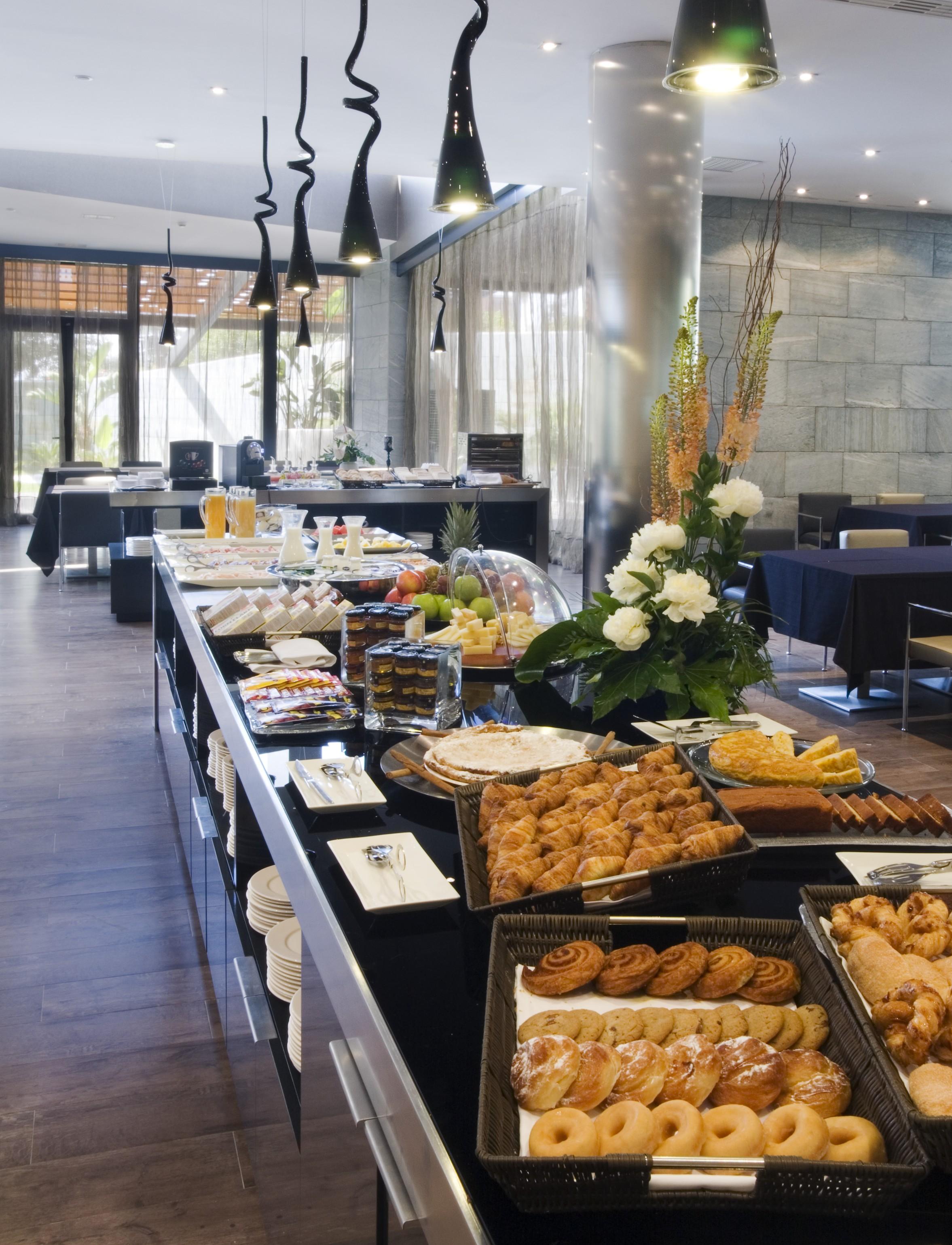 Eurostars Palace Cordoba Ngoại thất bức ảnh The photo shows a beautifully arranged buffet spread in a modern setting. There are various dishes displayed on a long table, including pastries, desserts, fruits, and baked goods. A decorative arrangement of flowers enhances the presentation. The ba