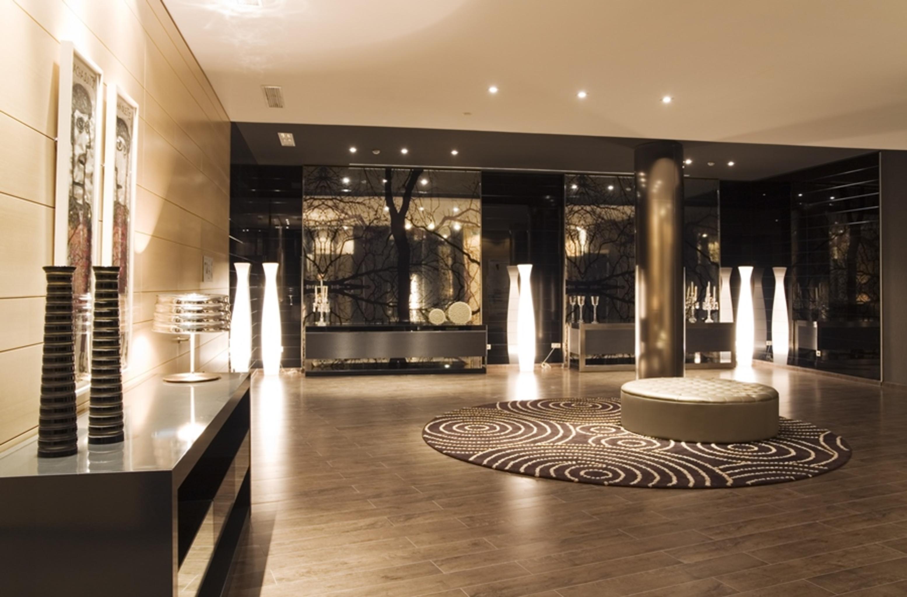 Eurostars Palace Cordoba Ngoại thất bức ảnh The photo shows a modern interior space, likely a lobby or waiting area. The design features polished wooden flooring and sleek surfaces. There are tall, artistic light fixtures scattered throughout, contributing to a sophisticated ambiance. A round 