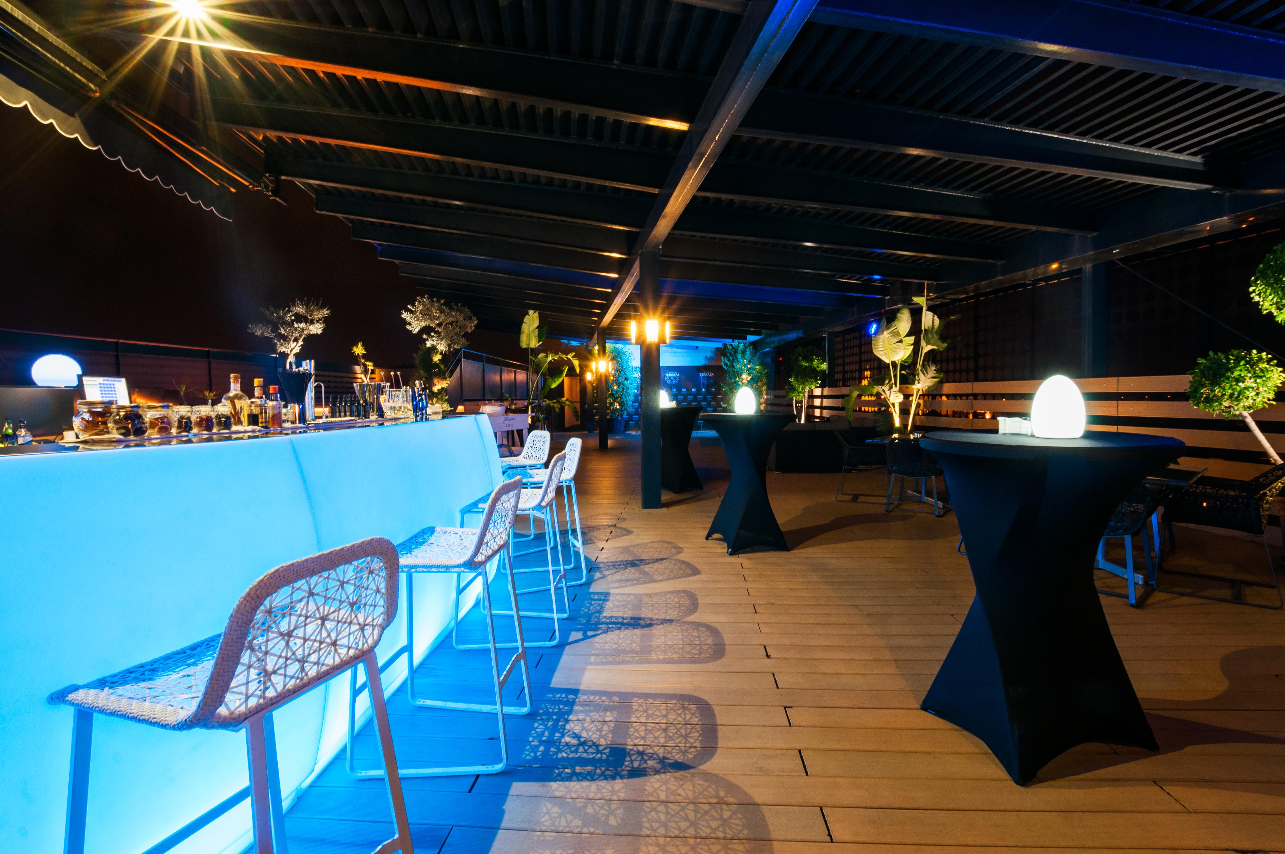 Eurostars Palace Cordoba Ngoại thất bức ảnh The photo shows a stylish rooftop or outdoor bar area. There is a long bar counter illuminated with blue lighting, complemented by modern bar stools. The space is decorated with potted plants and elegant round tables covered in black cloth. Soft ligh