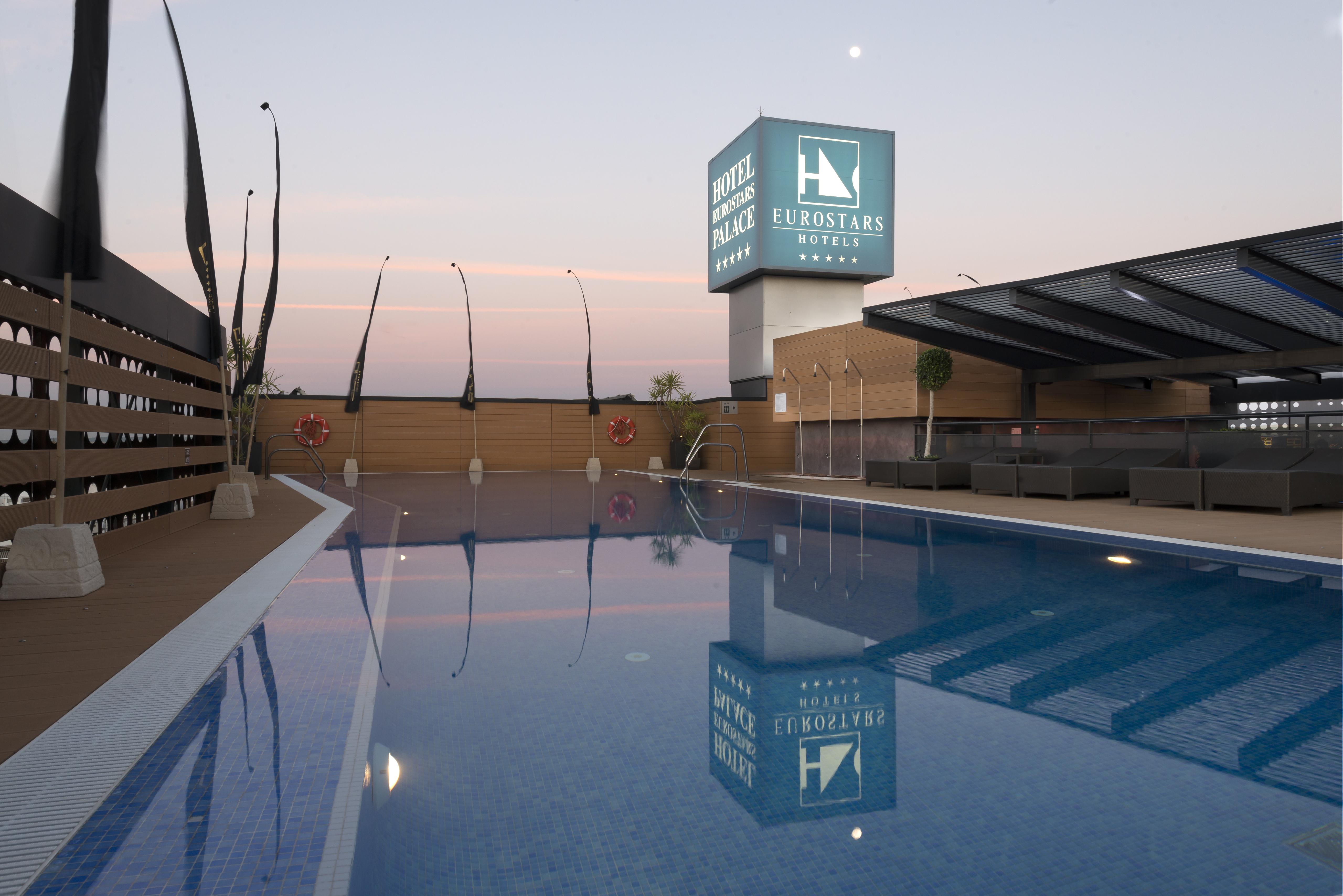 Eurostars Palace Cordoba Ngoại thất bức ảnh The photo shows a rooftop space featuring a swimming pool. The pool has a clear blue water, and the area around it is designed with modern aesthetics, including a wooden deck and comfortable seating. In the background, there is a prominent sign for "