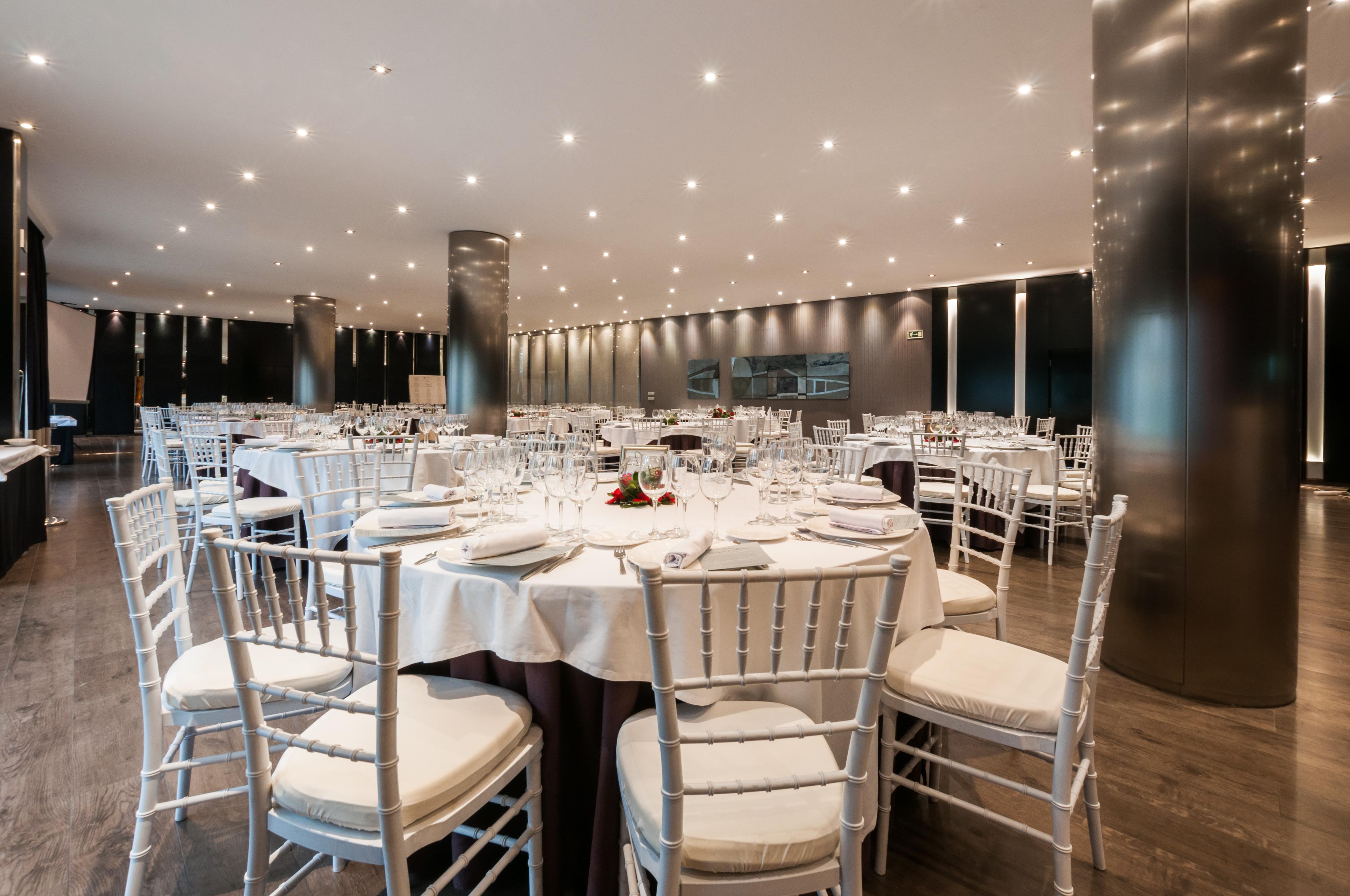Eurostars Palace Cordoba Ngoại thất bức ảnh The photo shows an elegant dining setting in a spacious restaurant. There are several round tables, each with white tablecloths and neatly arranged place settings, including glasses, plates, and utensils. The chairs are white with padded seats, provi