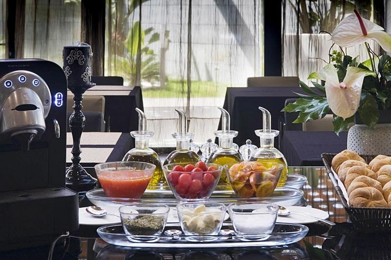 Eurostars Palace Cordoba Ngoại thất bức ảnh The photo displays a stylish breakfast or brunch spread on a table. In the foreground, several small glass containers hold various ingredients: there are glasses filled with different types of oil, a bowl of fresh red tomatoes, a bowl of mixed fruit,