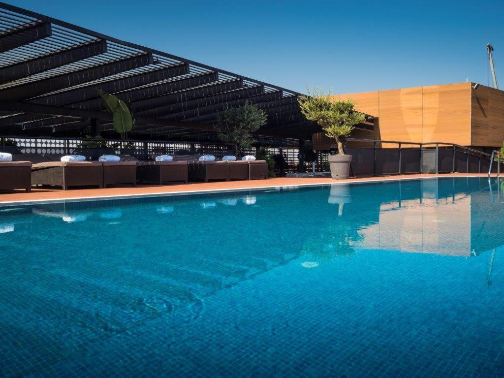 Eurostars Palace Cordoba Ngoại thất bức ảnh The photo shows a rooftop swimming pool with a clear, vibrant blue surface reflecting the sky. Surrounding the pool are comfortable lounge chairs, some shaded by a modern overhead structure. The area is accented with potted plants, adding greenery to