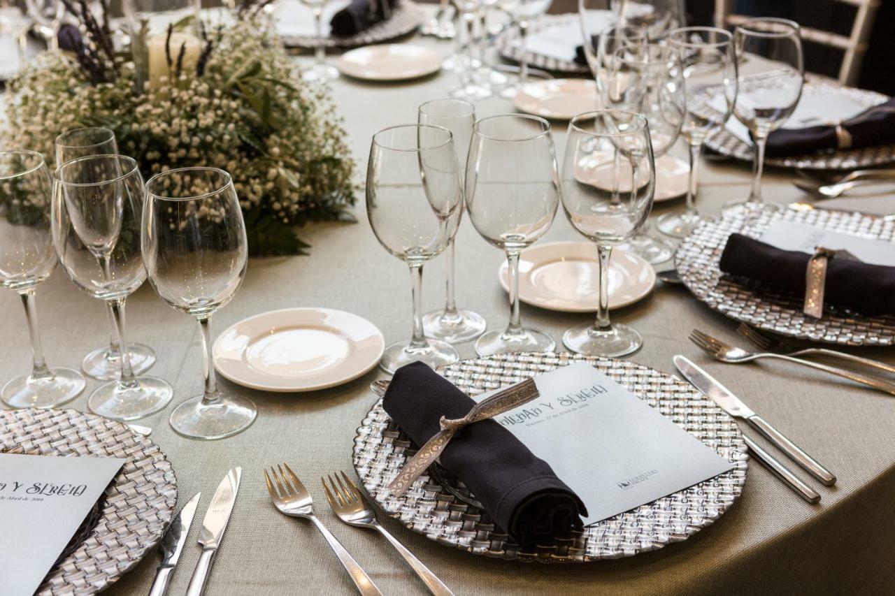 Eurostars Palace Cordoba Ngoại thất bức ảnh The photo shows a beautifully arranged dining table set for an event. The table has a neutral-colored tablecloth and is adorned with elegant place settings. Each setting features a decorative plate with a textured silver charger underneath, and a fol